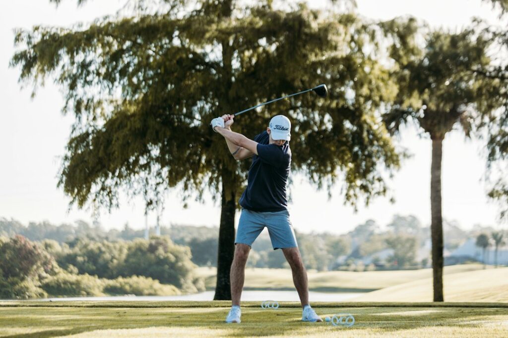 Golfer practicing a full swing on a green course before an after-golf massage