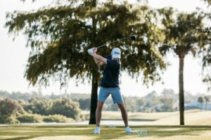 Golfer practicing a full swing on a green course before an after-golf massage